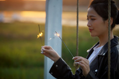 夕阳下湖畔秋千上燃放仙女棒的可爱少女