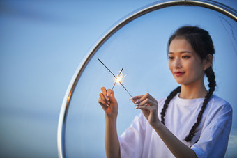 傍晚湖畔透明秋千上燃放仙女棒的可爱少女