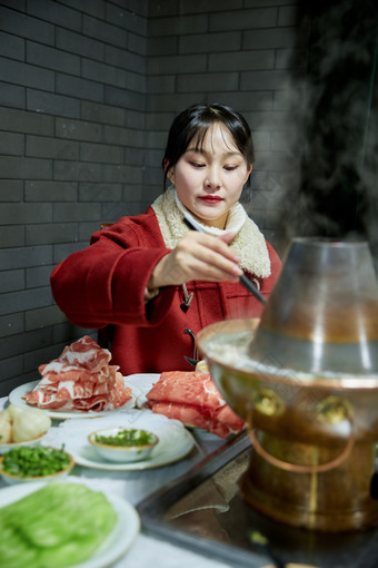 在饭店吃传统铜锅涮肉的亚洲少女