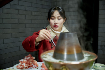 在饭店吃传统铜锅涮肉的亚洲少女