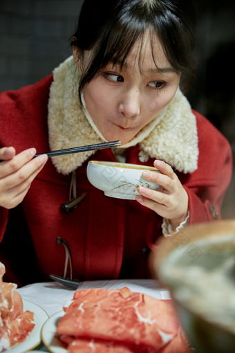 在饭店吃传统铜锅涮肉的亚洲少女