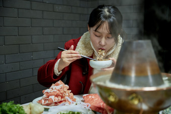 在饭店吃传统铜锅涮肉的亚洲少女