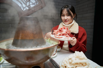 在饭店吃传统铜锅涮肉的亚洲少女