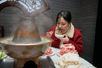 在饭店吃传统铜锅涮肉的亚洲少女