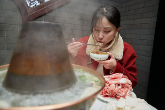 在饭店吃传统铜锅涮肉的亚洲少女