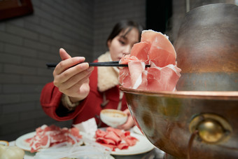 在饭店吃传统铜锅涮肉的亚洲少女