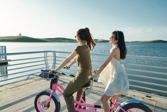 夕阳下湖边码头骑双人脚踏车的闺蜜少女