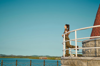 盛夏夕阳晚霞湖边码头灯塔上的少女