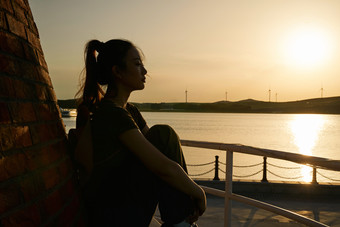 盛夏夕阳晚霞湖边码头灯塔上的少女