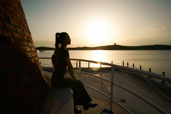盛夏夕阳晚霞湖边码头灯塔上的少女