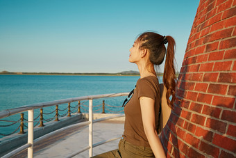 盛夏夕阳晚霞湖边码头灯塔上的少女