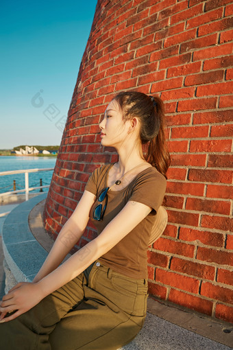 盛夏夕阳晚霞湖边码头灯塔上的少女