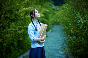 细雨中庭院里竹林前怀抱古书籍的民国风少女