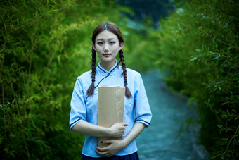 细雨中庭院里竹林前怀抱古书籍的民国风少女