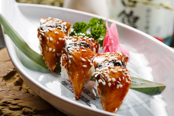 鹅颈白瓷盘装的烤鳗鱼手握寿司摆放在石头上