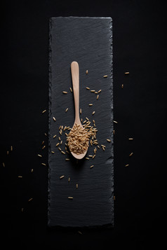 黑色青石板上的木质勺子装的燕麦米摆放在黑色背景中