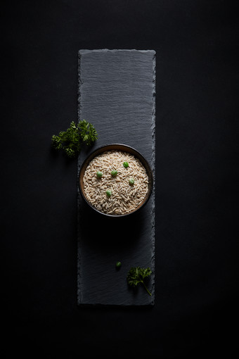 黑色青石板上的木质勺子装的燕麦米摆放在黑色背景中