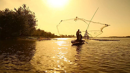 夕阳下渔民湖边撒网捕鱼