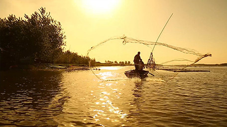 夕阳下渔民湖边撒网捕鱼