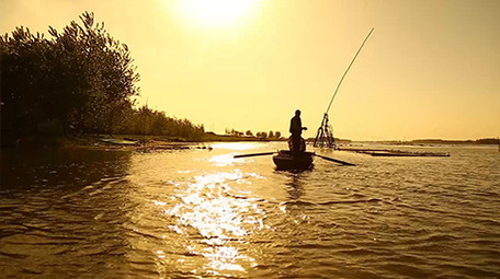 夕阳下渔民湖边撒网捕鱼