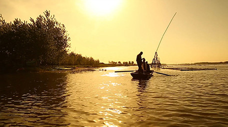 夕阳下渔民湖边撒网捕鱼