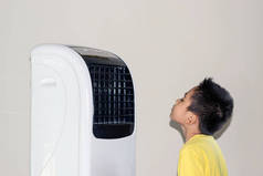 由于天气炎热, 男孩站在风扇上, 把冷空气吹到他的脸上。.