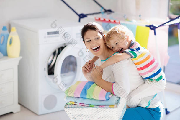 母亲和孩子在洗衣房里用洗衣机或滚筒烘干机。家庭琐事。现代家庭设备和洗涤洗涤剂在白色阳光的家。烘干机架清洗洗衣服.