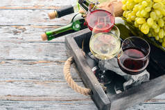 在瓶子和玻璃杯中设置红酒和白酒。葡萄。在白色的木质背景。文本的可用空间。顶部视图.