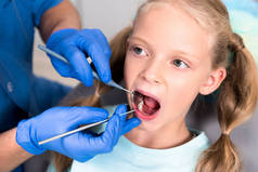 裁剪的牙医与工具检查小孩子的牙齿