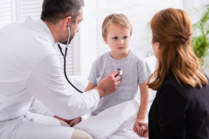 在白色外套的儿科医生检查生病的男孩与听诊