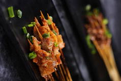 Grilled barbecue sticks in a black ceramic dish