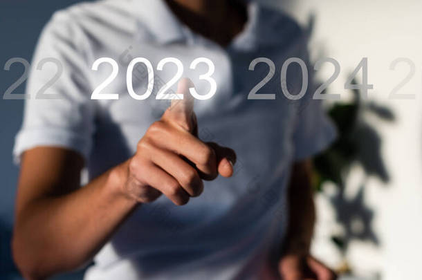 手指在灰色背景的虚拟界面上按蓝色启动2023按钮，并为文本提供复制空间。新年的概念。商人在2023年开业。新春2023年开始