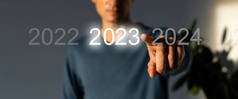 手指在灰色背景的虚拟界面上按蓝色启动2023按钮，并为文本提供复制空间。新年的概念。商人在2023年开业。新春2023年开始