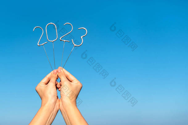 在晴朗的天空背景下，妇女手中掌握着即将到来的<strong>2023</strong>年新年的数字。复制空间