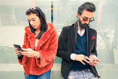 时髦夫妇在悲伤的时刻，忽略对方使用手机-冷漠悲伤沉迷于新技术的概念-男朋友和女朋友分手与智能手机上瘾