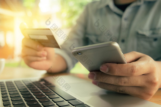 网上支付，男人的手拿着<strong>信用卡</strong>，用智能手机在晨光下网上购物。复古过滤效果.