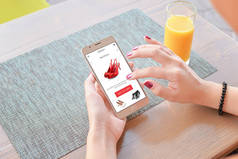 女人在网上买红鞋。移动应用程序或网站在屏幕上。背景表和果汁.