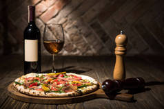意大利比萨、研磨香料、瓶子和葡萄酒在木制桌面上的选择性聚焦