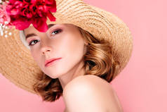 华丽的年轻女子的肖像在帽子与美丽的花朵看着相机孤立的粉红色