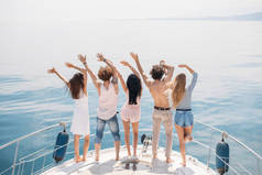 朋友们在远洋的帆船上欢庆的后视镜，举起双臂.