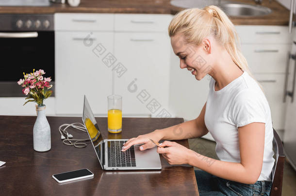 微笑的年轻妇女持有<strong>信用卡</strong>和使用笔记本电脑在家里的侧面视图