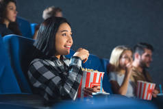 情绪化亚洲妇女与爆米花看电影在电影院