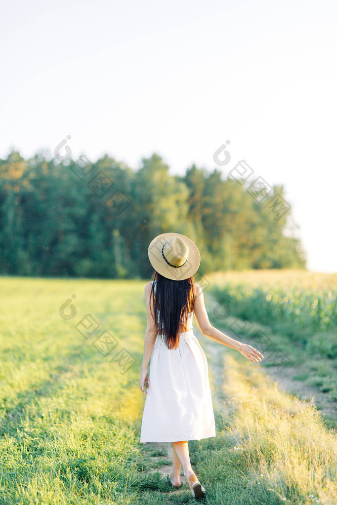 女孩走在田野上在帽子和夏季礼服微笑和欢笑