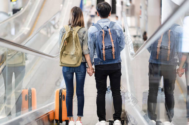 愉快的爱亚洲夫妇旅行与行李下车的自动扶梯到机场的出发区。情人旅行和运输概念.
