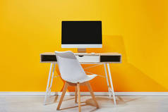 在木桌上有空白屏幕的电脑, 椅子靠近黄色墙壁