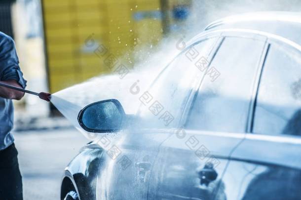 汽车电源清洗。男子用强大的压力清洗机清洗他的汽车.
