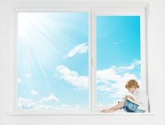 窗口阳光的天空。在窗台上看书的孩子.