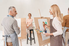 艺术工作室中的高级艺术家绘画和互相看