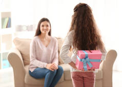 小女孩隐藏在她背后的礼物盒在她后面的室内。母亲节庆典