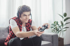 青少年用耳机玩视频游戏与手柄在家里